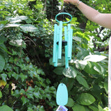 Someone holding the Monochrome Cyan Bells of Paradise Wind Chime in front of a green bush.