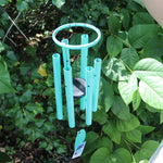 Someone holding the Monochrome Cyan Bells of Paradise Wind Chime in front of a green bush.