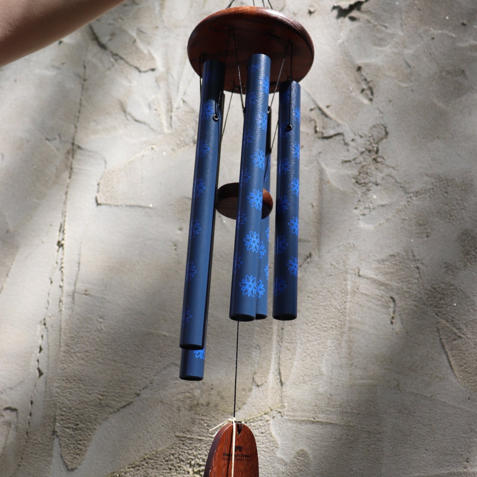 The Woodstock Dahlia Garden Wind Chime in front of a cement wall.