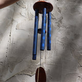 The Woodstock Dahlia Garden Wind Chime in front of a cement wall.