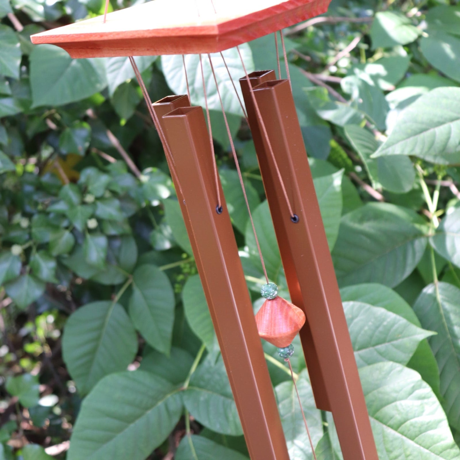 Someone holding the Medium Turquoise Woodstock Wind Chime in front of a green bush.