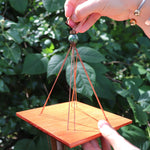 An up-close image of the top of the Medium Turquoise Woodstock Wind Chime in front of a green bush.