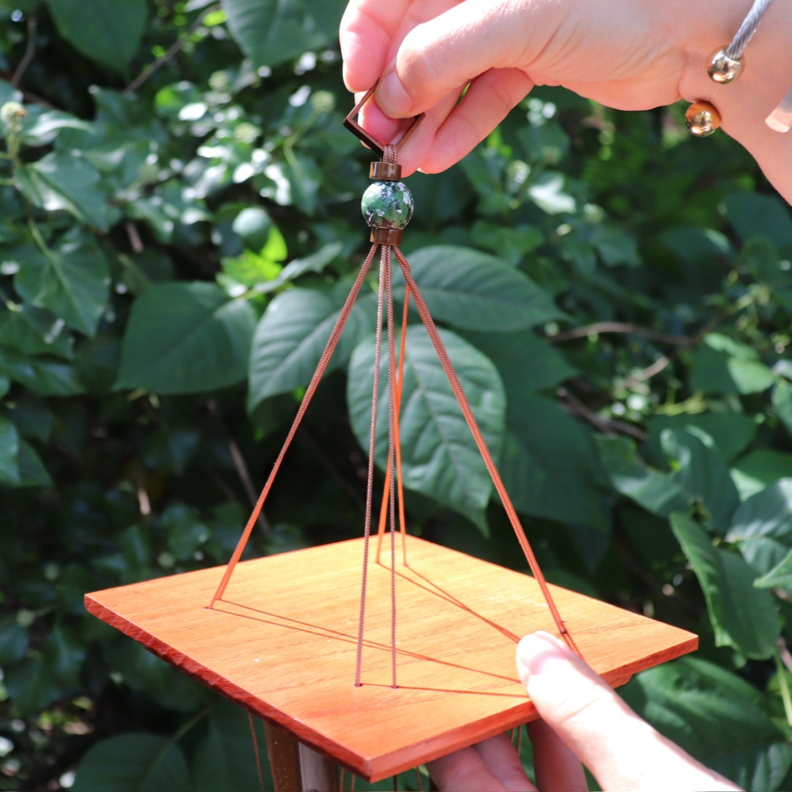An up-close image of the top of the Medium Turquoise Woodstock Wind Chime in front of a green bush.