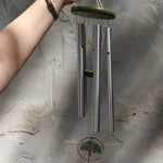 Someone holding the Rainbow Tree of Life Woodstock Wind Chime in front of a white wall.
