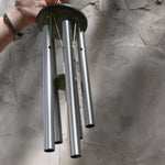 Someone holding the Rainbow Tree of Life Woodstock Wind Chime in front of a white wall.