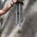 Someone holding the Rainbow Tree of Life Woodstock Wind Chime in front of a white wall.