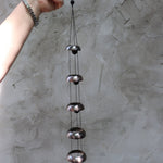 Someone holding the Copper Quintet Woodstock Temple Bells Wind Chime in front of a concrete wall.