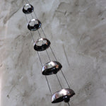 Someone holding the Copper Quintet Woodstock Temple Bells Wind Chime in front of a concrete wall.