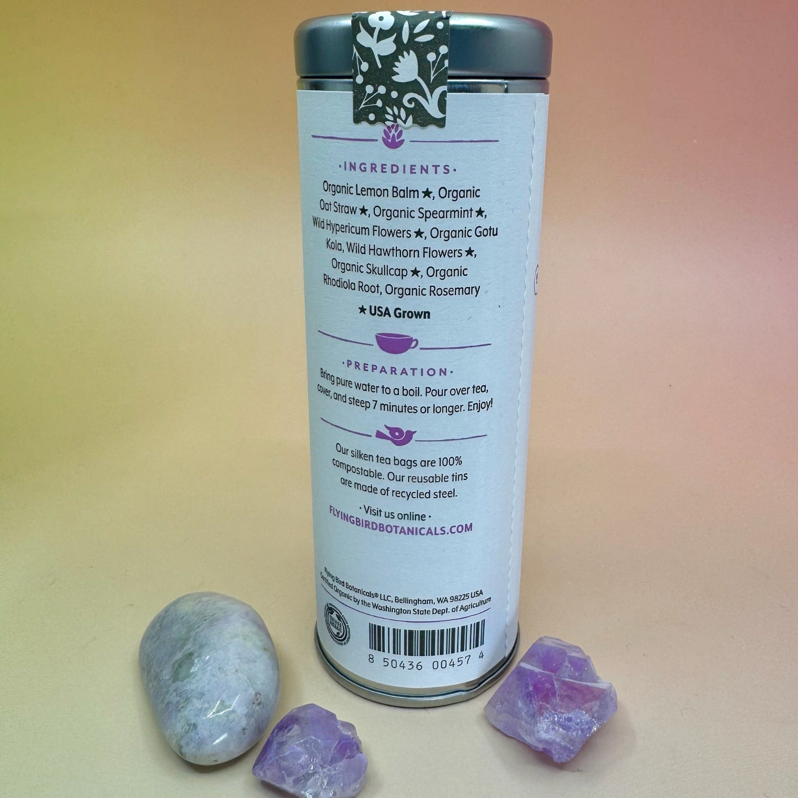 The Peaceful Spirit 6 Tea Bag Tin on a pink and yellow background surrounded by small crystals, showing off the back.