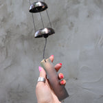 Someone holding the bottom of the Copper Quintet Woodstock Temple Bells Wind Chime in front of a concrete wall.