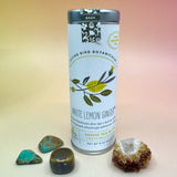The White Lemon Ginger 6 Tea Bag Tin on a pink and yellow background surrounded by different small crystals.