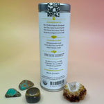 The White Lemon Ginger 6 Tea Bag Tin on a pink and yellow background surrounded by different small crystals, showing off the back.