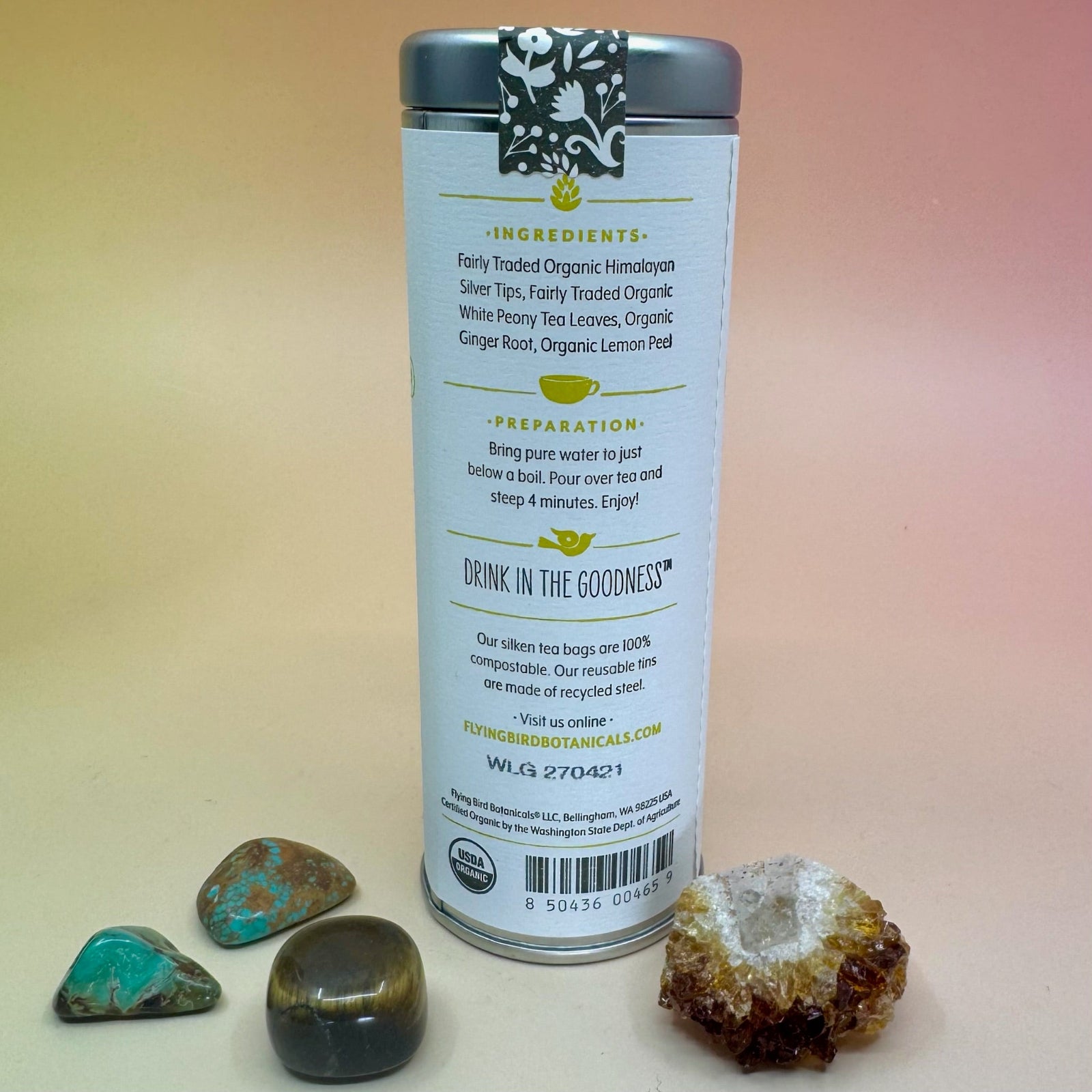 The White Lemon Ginger 6 Tea Bag Tin on a pink and yellow background surrounded by different small crystals, showing off the back.