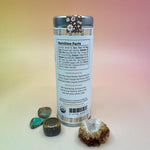 The Vanilla Orange Cacao Small Tin on a pink and yellow background surrounded by small crystalsing off the back.