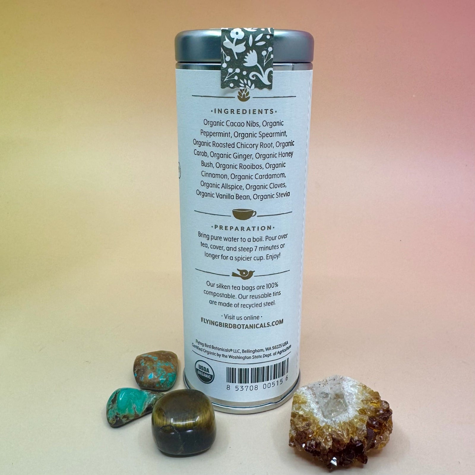 The Winter Cheer 6 Tea Bag Tin on a pink and yellow background  surrounded by different small crystals, showing off the back.