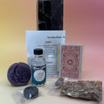 The contents of the New Moon Ritual Kit in front of a crystal tower on a pink and yellow background.