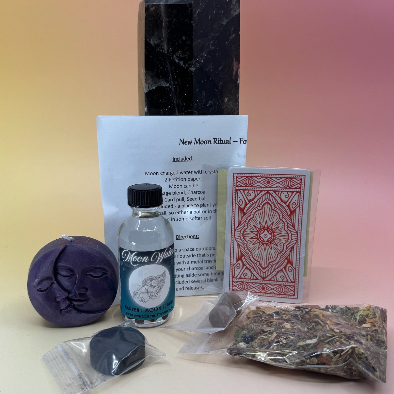 The contents of the New Moon Ritual Kit in front of a crystal tower on a pink and yellow background.