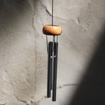 The Silver Piccolo Woodstock Wind Chime hanging in front of a white cement wall,