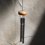 The Silver Piccolo Woodstock Wind Chime hanging in front of a white cement wall,