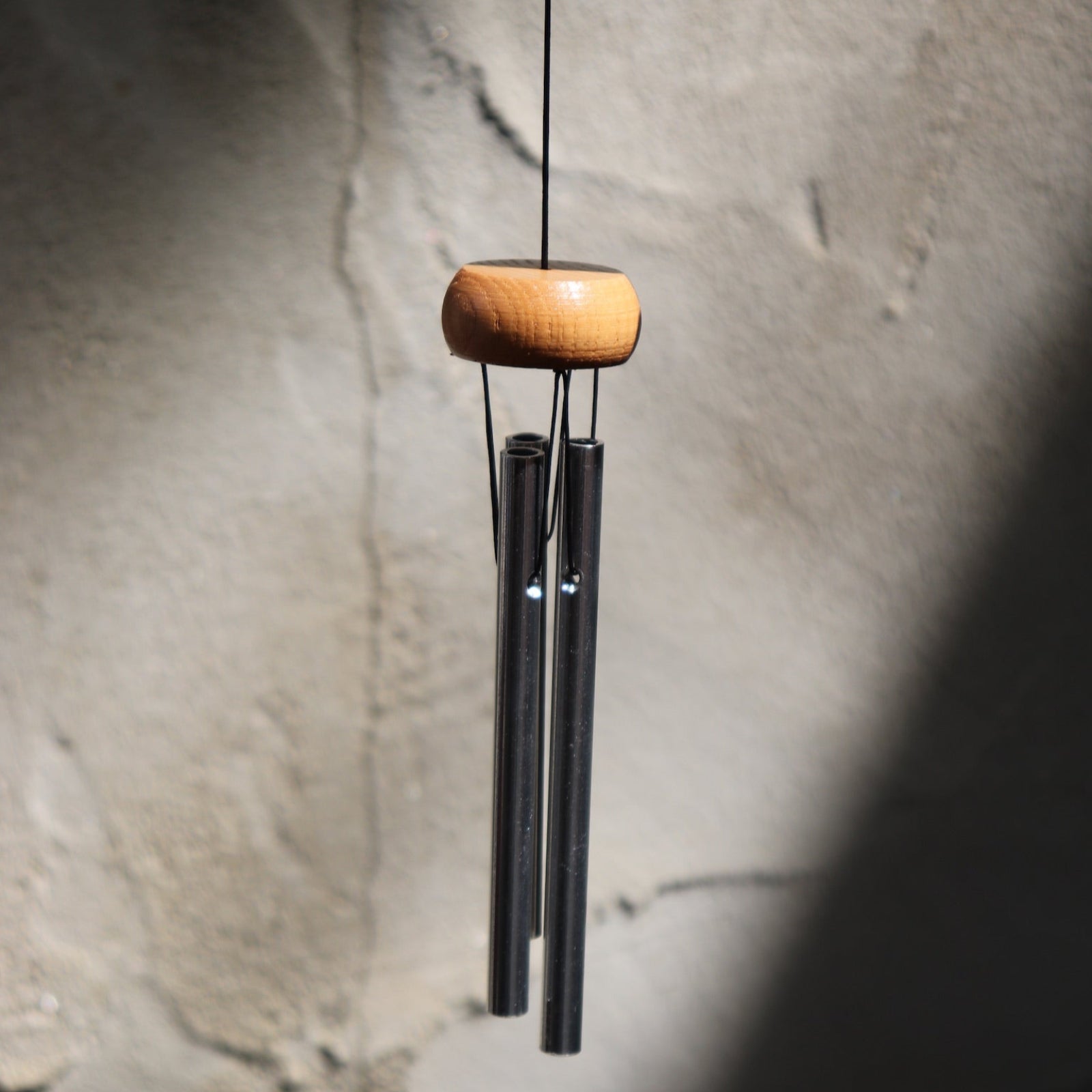 The Silver Piccolo Woodstock Wind Chime hanging in front of a white cement wall,