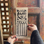 Someone holding the 2026 Moon Phase Calendar in front of a wooden background.