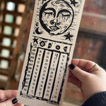 Someone holding the 2026 Moon Phase Calendar in front of a wooden background.