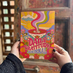 Someone holding a Daily Gratitude Journal in front of a wooden background.