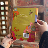 Someone holding a Daily Gratitude Journal in front of a wooden background, showing off the back.