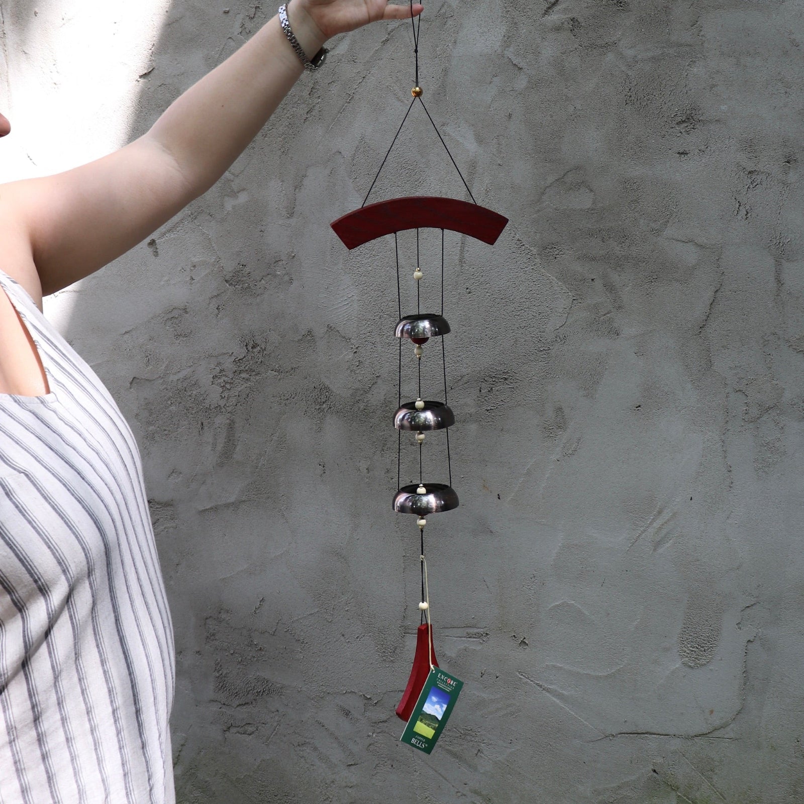 Someone holding theEncore Copper Temple Bells in front of a white concrete wall.
