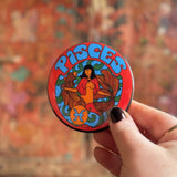 Someone holding the Pisces Astral Weekend Zodiac Magnet 3" Round in front of a wooden background.