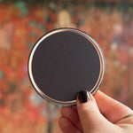 Someone holding an Astral Weekend Zodiac Magnet 3" Round in front of a wooden background, showing off the back.