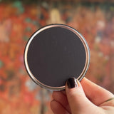 Someone holding an Astral Weekend Zodiac Magnet 3" Round in front of a wooden background, showing off the back.