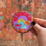 Someone holding the Cancer Astral Weekend Zodiac Magnet 3" Round in front of a wooden background.