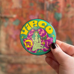 Someone holding the Virgo Astral Weekend Zodiac Magnet 3" Round in front of a wooden background.