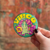Someone holding the Virgo Astral Weekend Zodiac Magnet 3" Round in front of a wooden background.