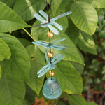 Someone holding the Verdigris Dragonfly Woodstock Habitats Windbell in front of a green bush.