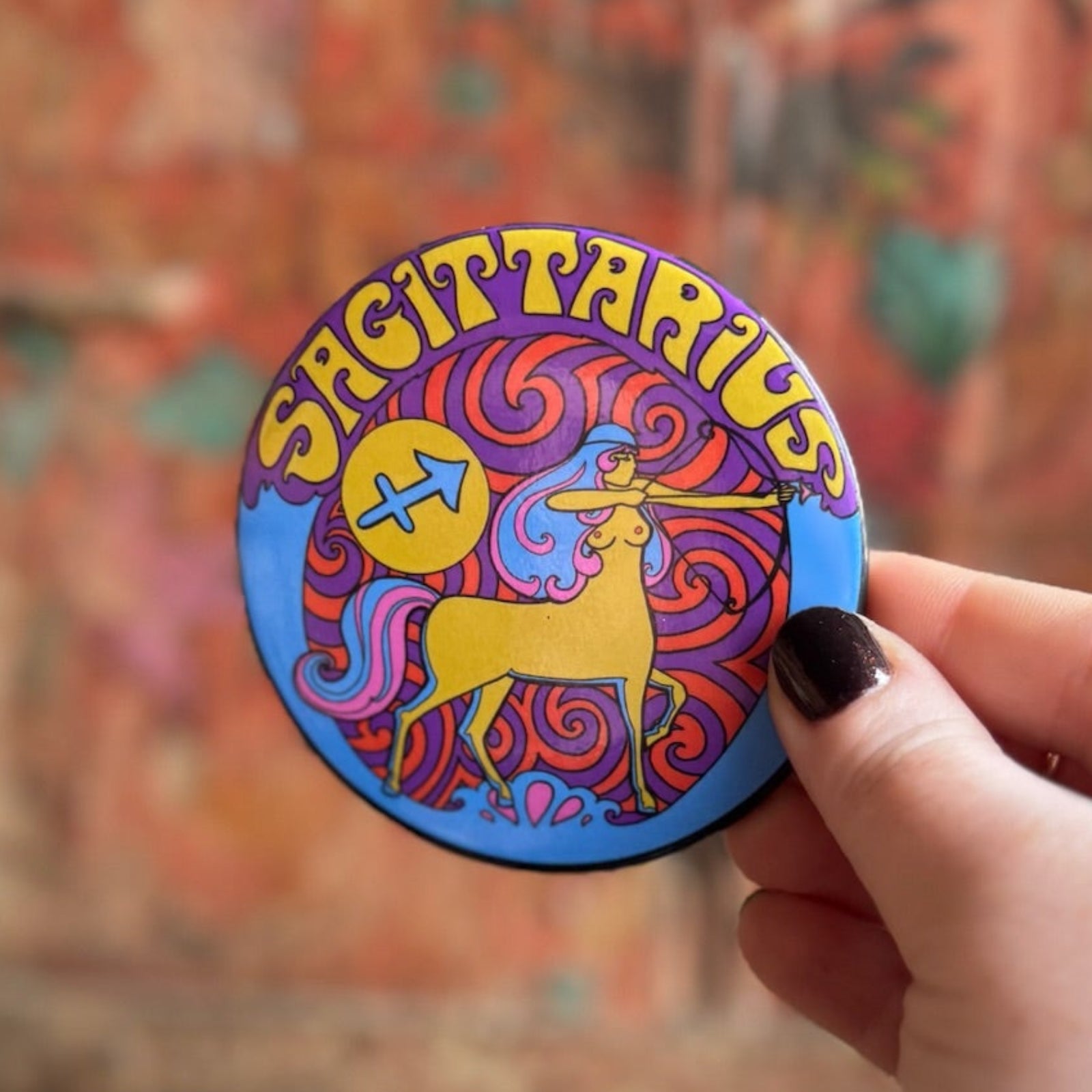 Someone holding the Sagittarius Astral Weekend Zodiac Magnet 3" Round in front of a wooden background.