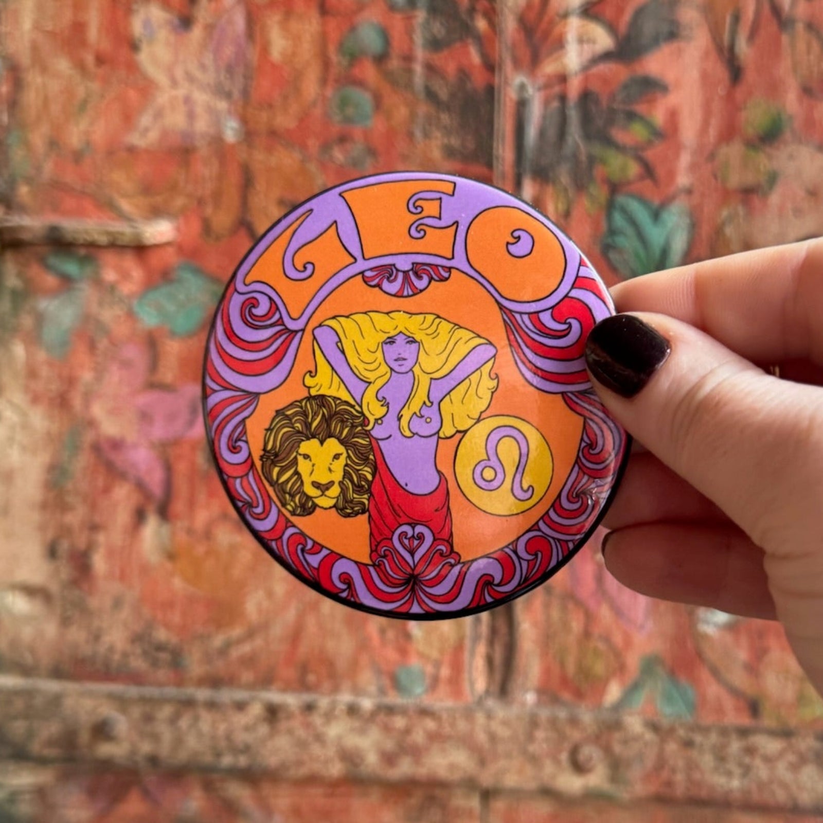 Someone holding the Leo Astral Weekend Zodiac Magnet 3" Round in front of a wooden background.