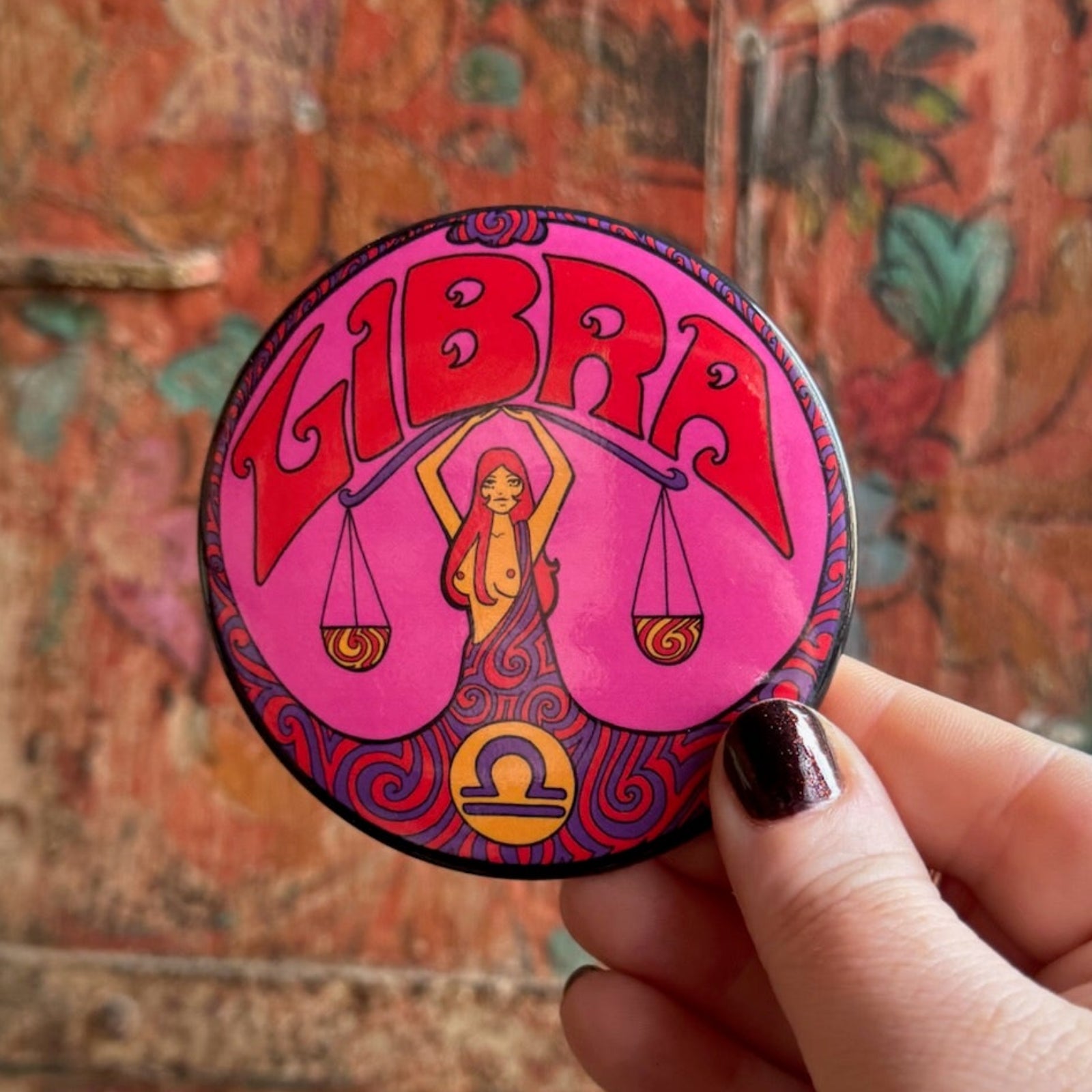 Someone holding the Libra Astral Weekend Zodiac Magnet 3" Round in front of a wooden background.