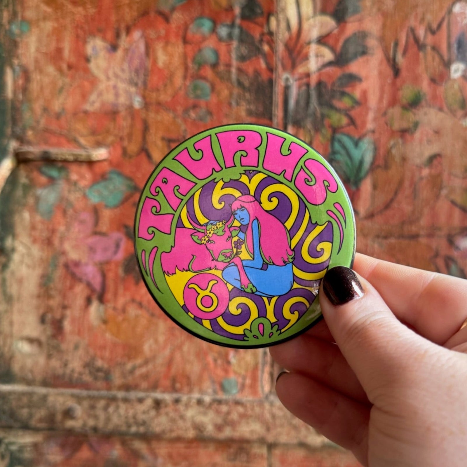 Someone holding the Taurus Astral Weekend Zodiac Magnet 3" Round in front of a wooden background.