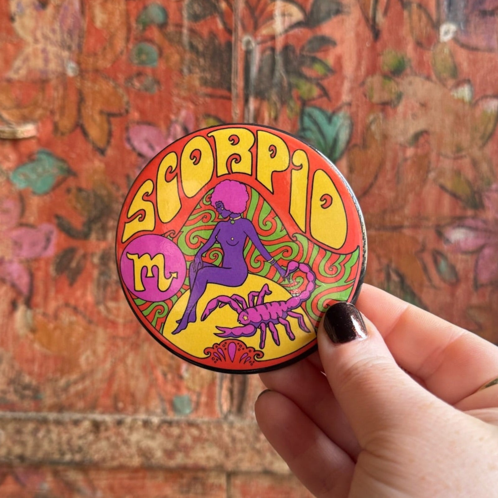 Someone holding the Scorpio Astral Weekend Zodiac Magnet 3" Round in front of a wooden background.