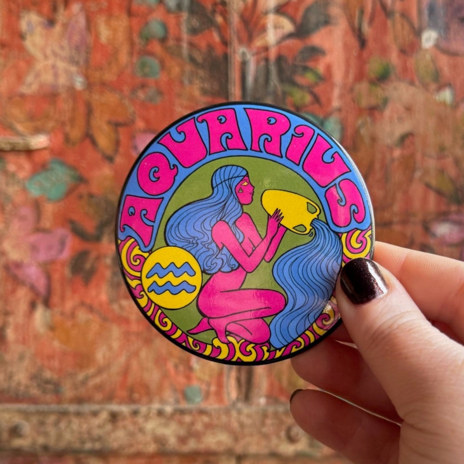 Someone holding the Aquarius Astral Weekend Zodiac Magnet 3" Round in front of a wooden background.