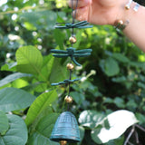 Someone holding the Verdigris Dragonfly Woodstock Habitats Windbell in front of a green bush.