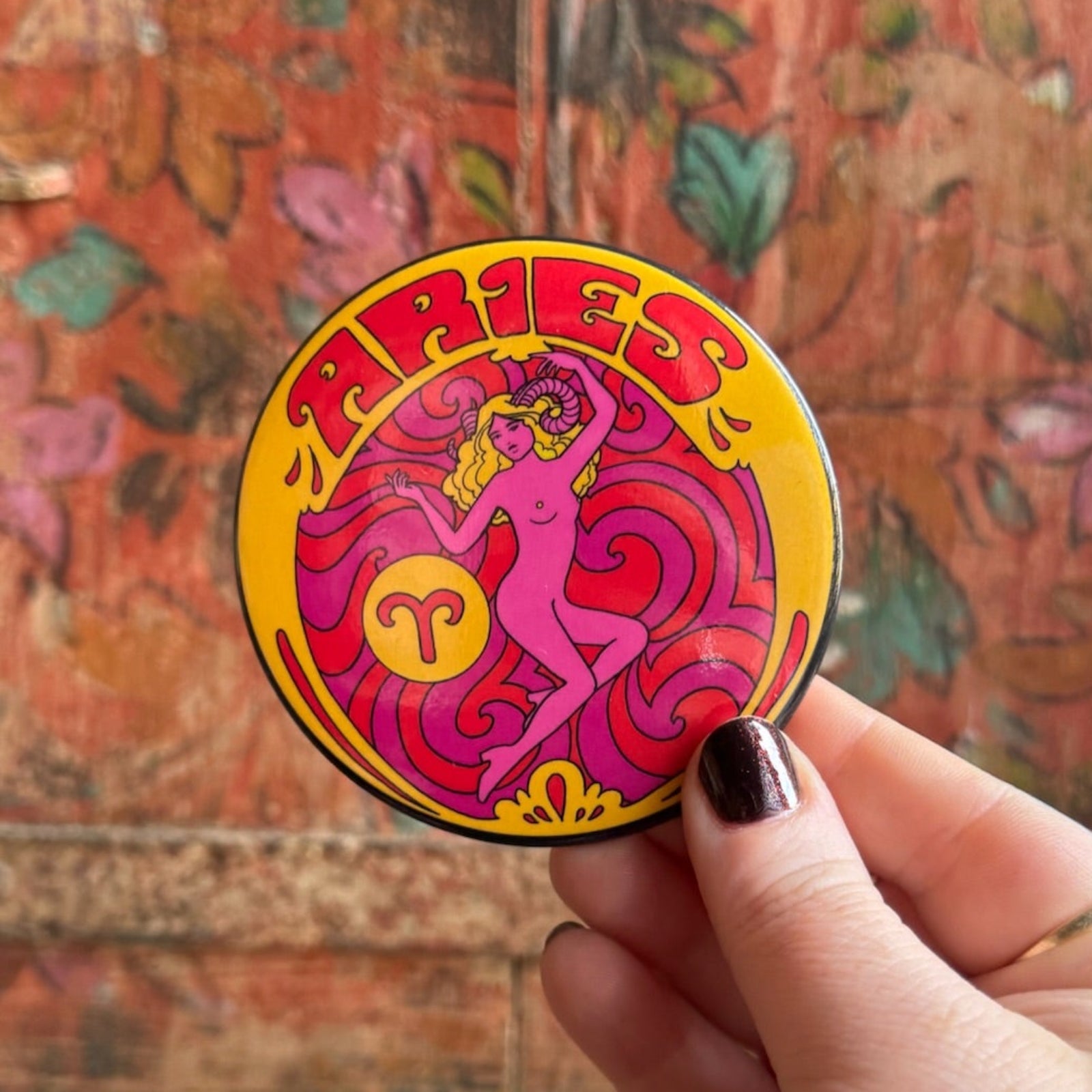 Someone holding the Aries Astral Weekend Zodiac Magnet 3" Round in front of a wooden background.
