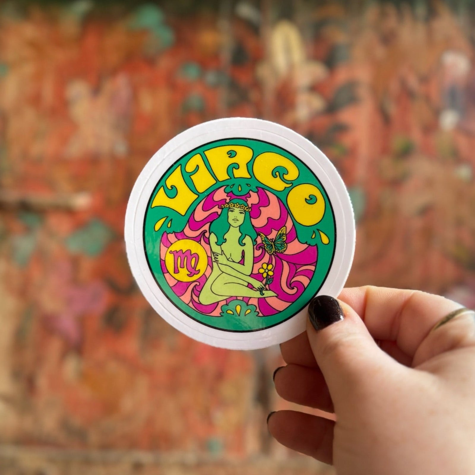 Someone holding the Virgo Zodiac 3 Inch Sticker in front of a wooden background.