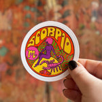Someone holding the Scorpio Zodiac 3 Inch Sticker in front of a wooden background.