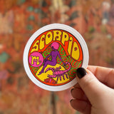 Someone holding the Scorpio Zodiac 3 Inch Sticker in front of a wooden background.