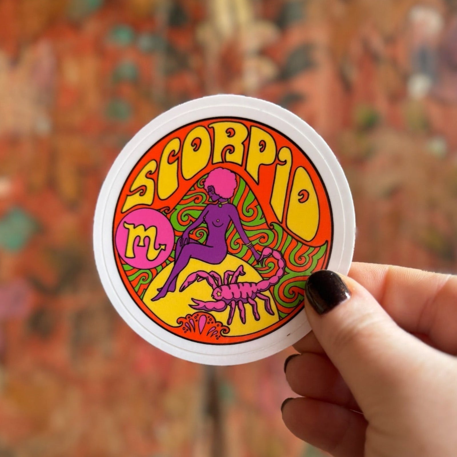 Someone holding the Scorpio Zodiac 3 Inch Sticker in front of a wooden background.