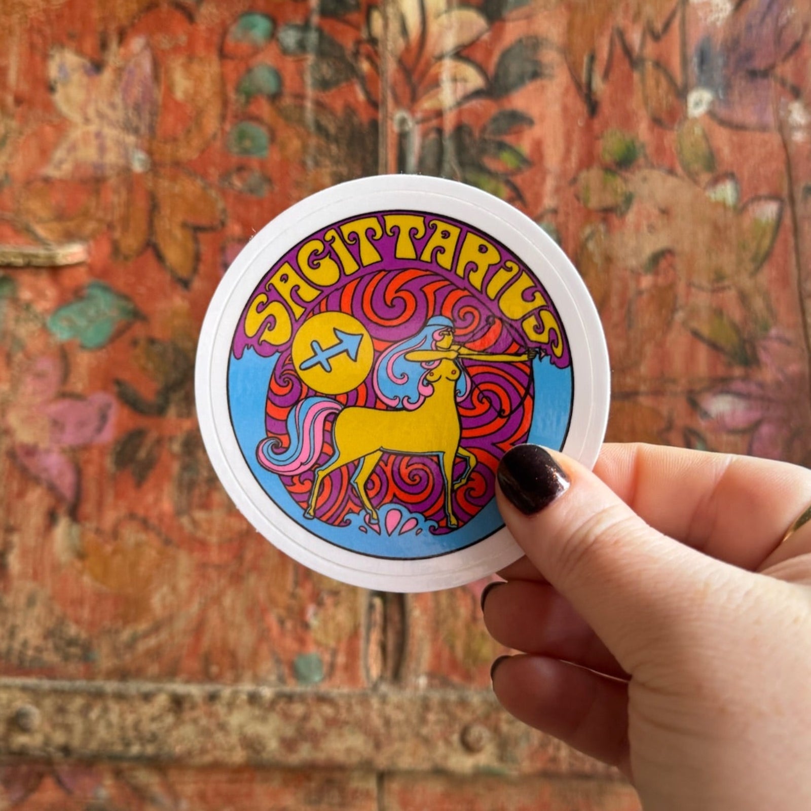 Someone holding the Sagittarius Zodiac 3 Inch Sticker in front of a wooden background.