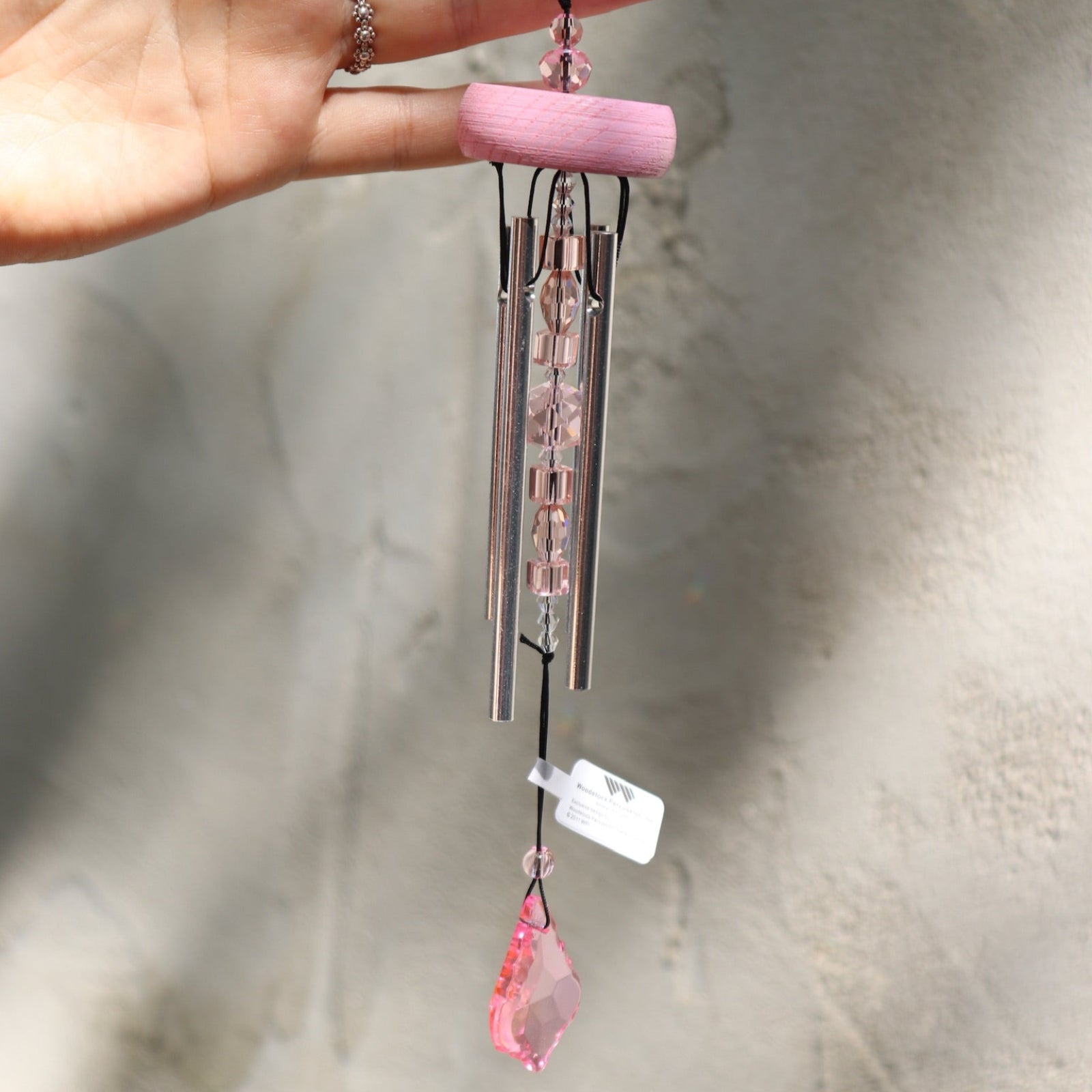 Someone holding the Rose Gem Drop Wind Chime in front of a white cement wall.